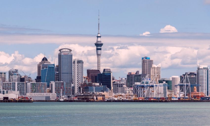 Auckland city skyline with Sky Tower, waterfront, and modern buildings under partly cloudy sky