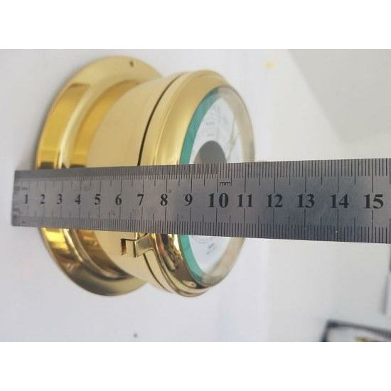 Brass wall-mounted barometer measured with a metal ruler, nautical weather instrument