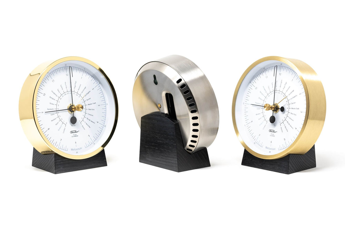 Modern world time clock with brass casing on black wooden stand, white dial face, three angles