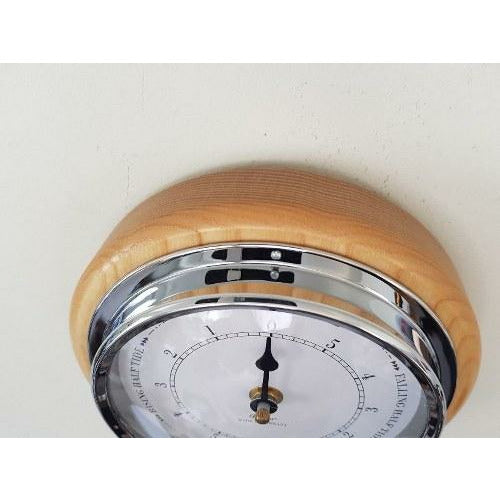 Wall-mounted tide clock with chrome bezel and light wood frame, displaying high tide.