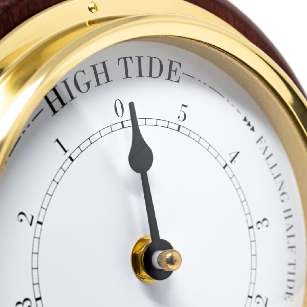 Close-up of a tide clock with gold bezel, showing high tide indicator and black hand.
