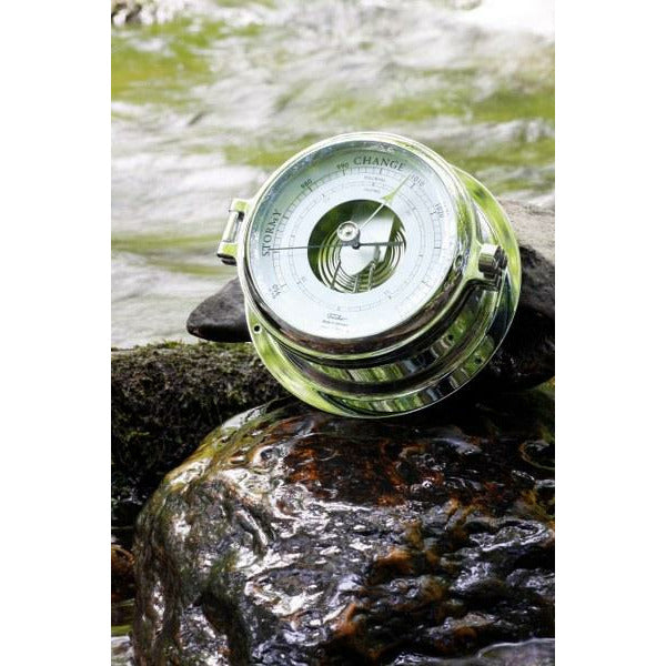 Chrome nautical barometer on wet rocks near water, weather instrument for marine use