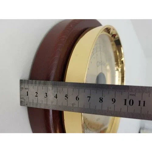 Close-up of wall-mounted barometer with gold bezel, wooden base, and ruler for size reference