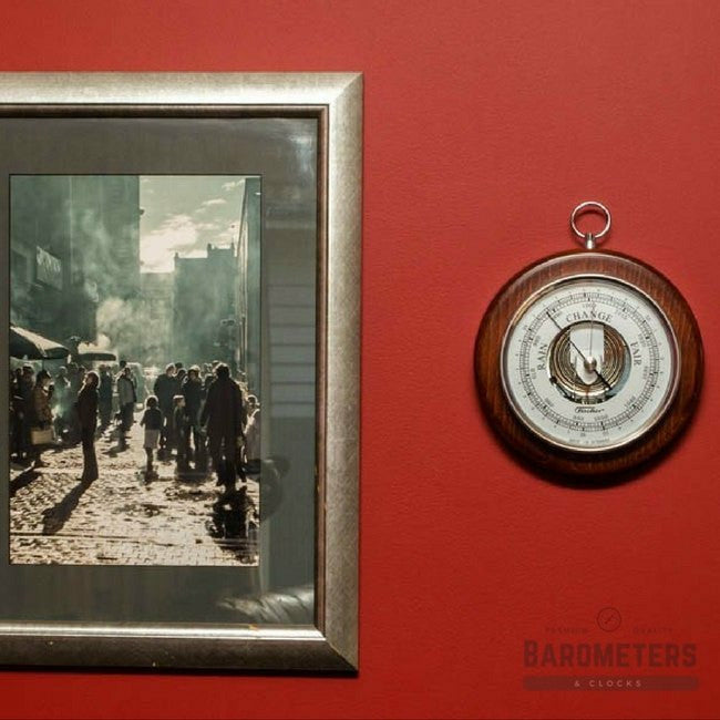 Wall-mounted round wood barometer beside framed photo on red wall, home decor