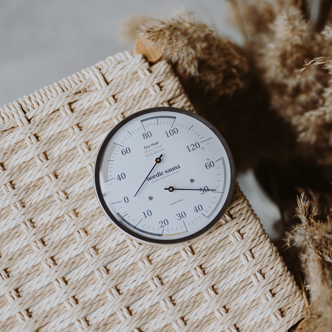 Round sauna thermometer and hygrometer on woven surface, measures temperature and humidity.