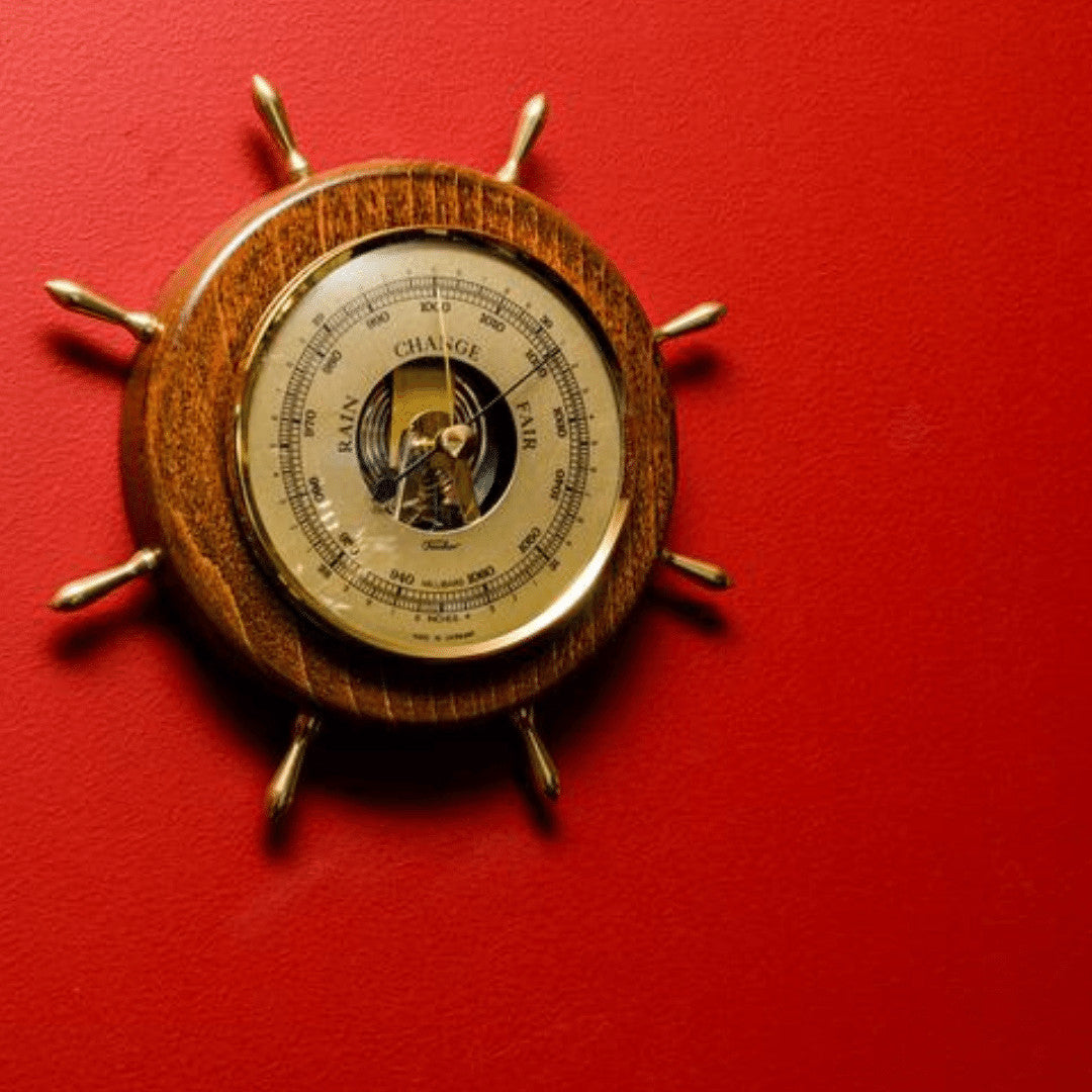 Wooden nautical barometer shaped like a ship's wheel on a red wall