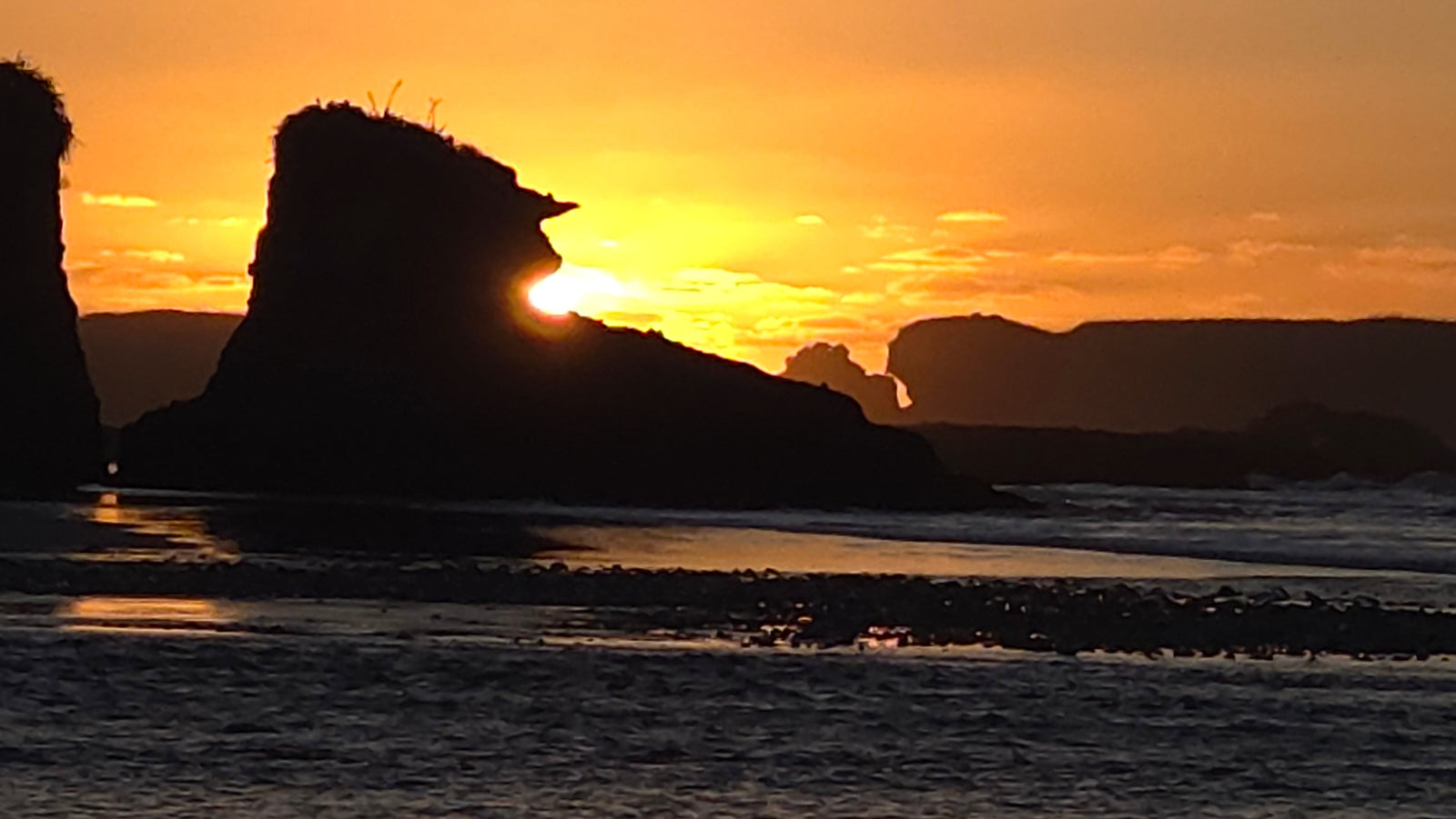 Rocky coastal silhouette at sunset with ocean waves and golden sky
