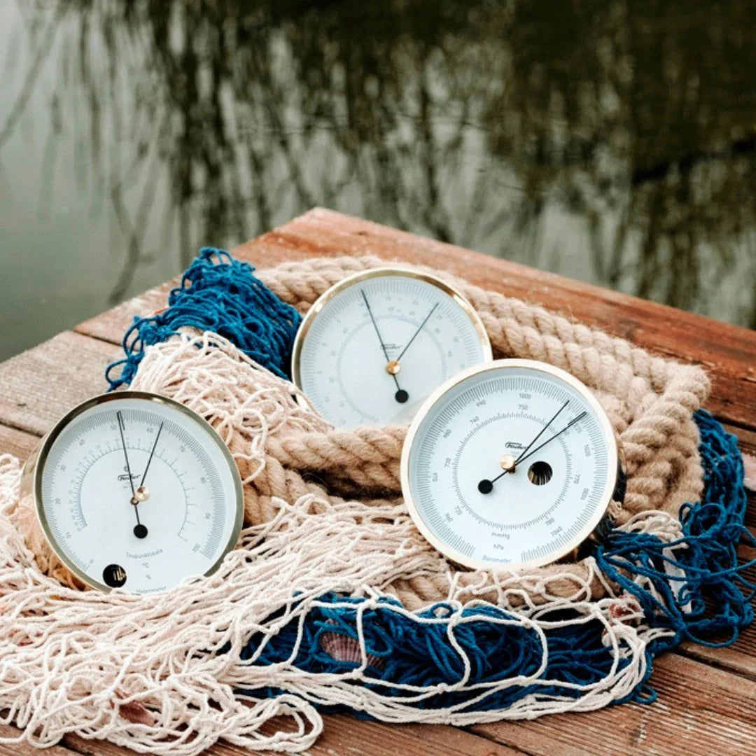 Three round silver barometers and clocks on nautical rope by water, weather instruments