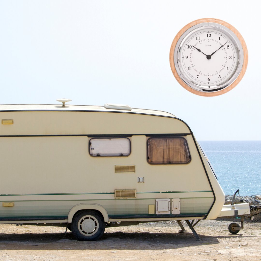 Round wall clock with wooden frame beside a caravan by the sea, clear blue sky background