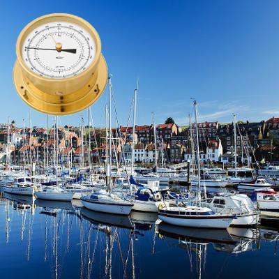 Brass nautical barometer over marina with yachts and waterfront buildings
