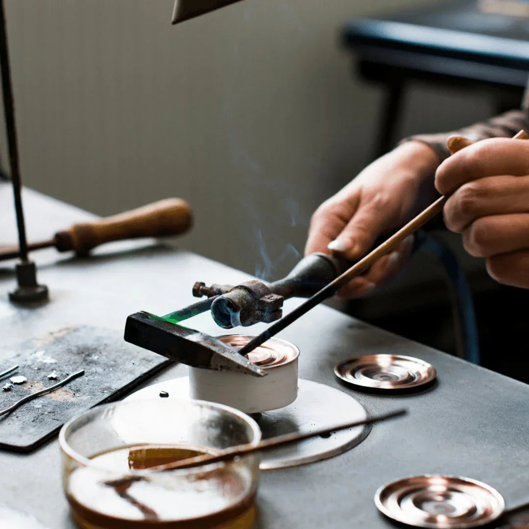 Craftsman assembling barometer or clock components at a workshop table with tools.