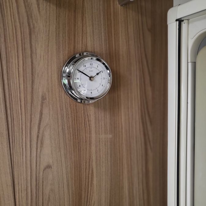 Wall-mounted nautical clock with chrome bezel on wood panel, precision timepiece decor